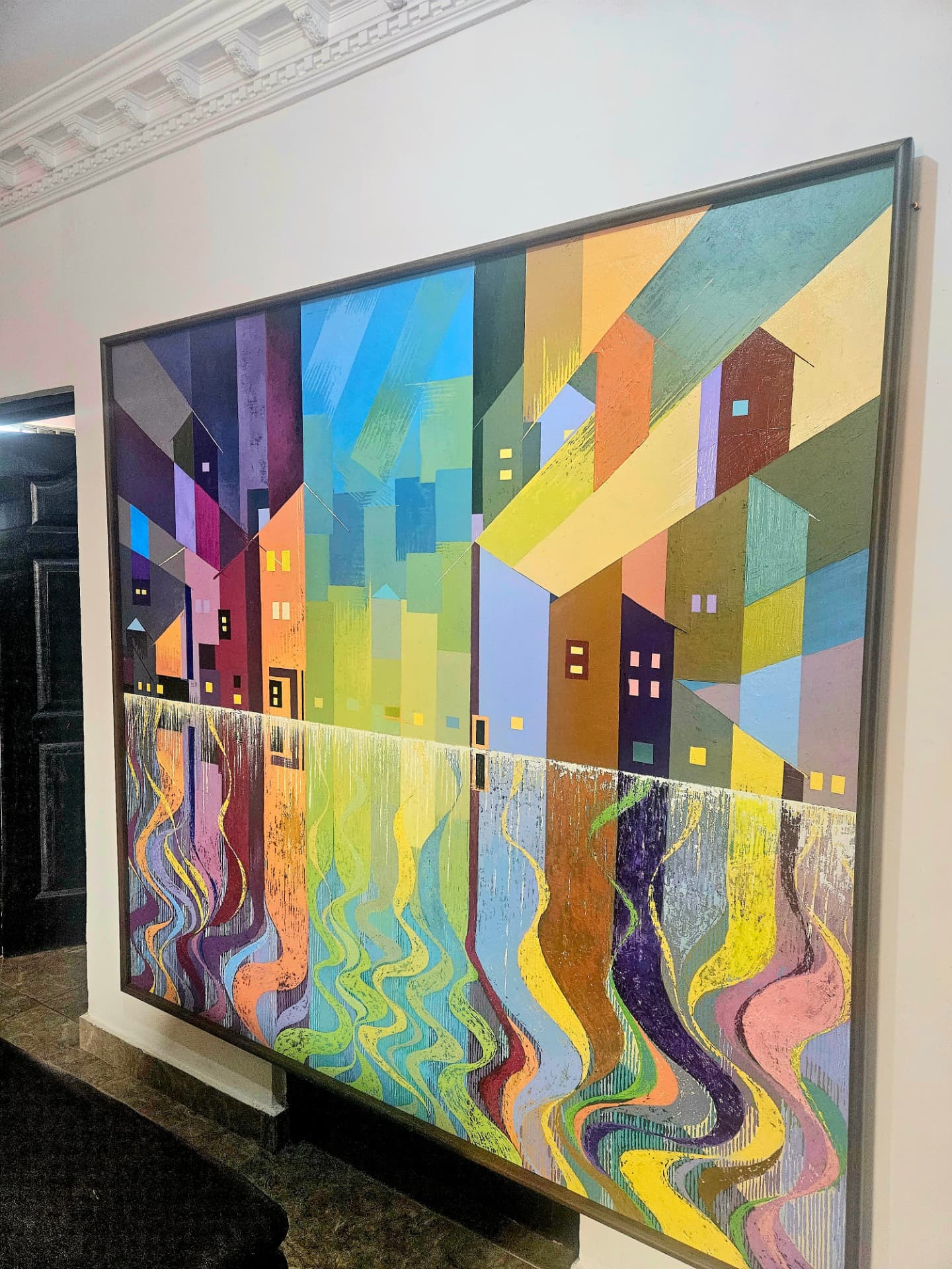 Framed geometric cityscape painting by Kizito Nii Amarh Amartey on display
